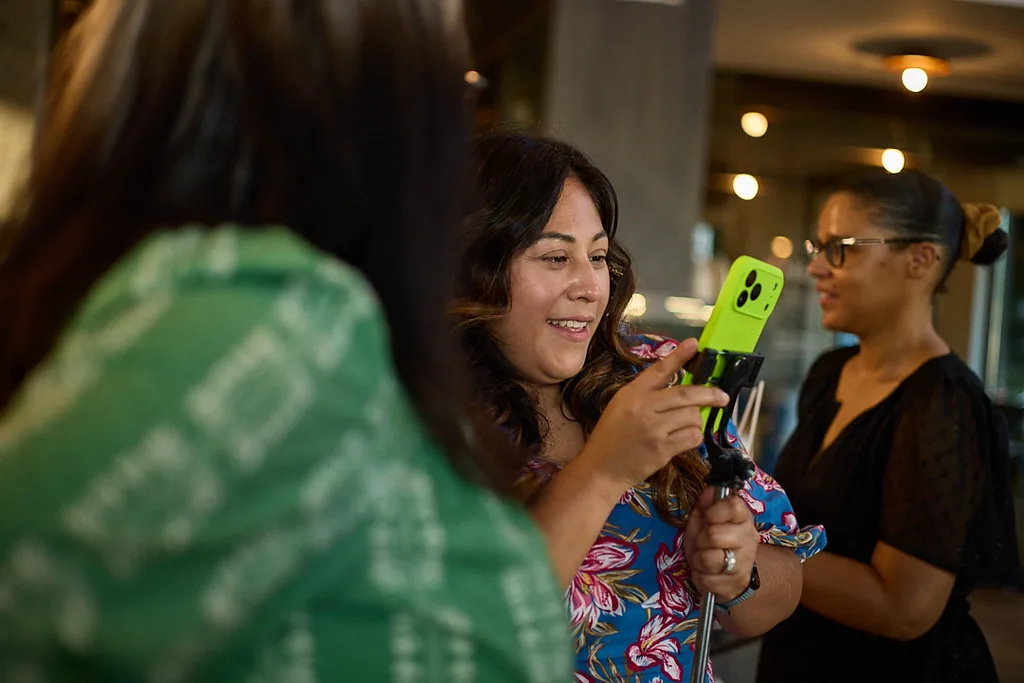 A woman smiling as she films herself on her phone at a content session